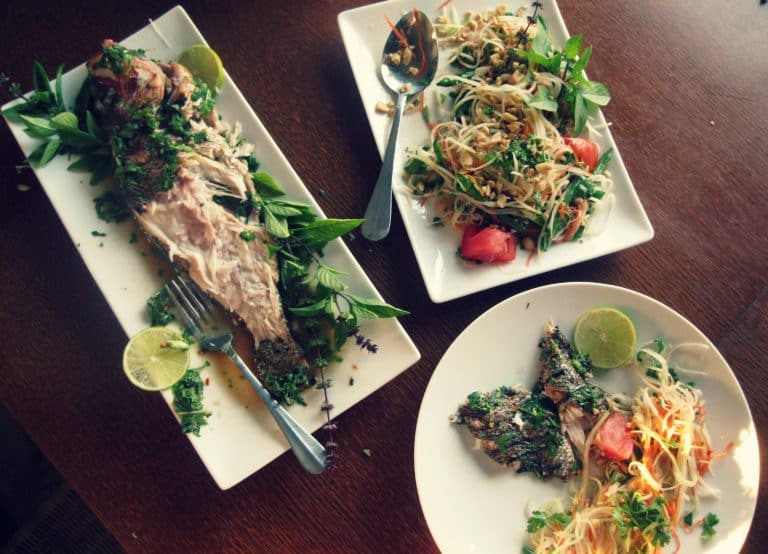 A table with plates of food including a whole grilled fish and salad.
