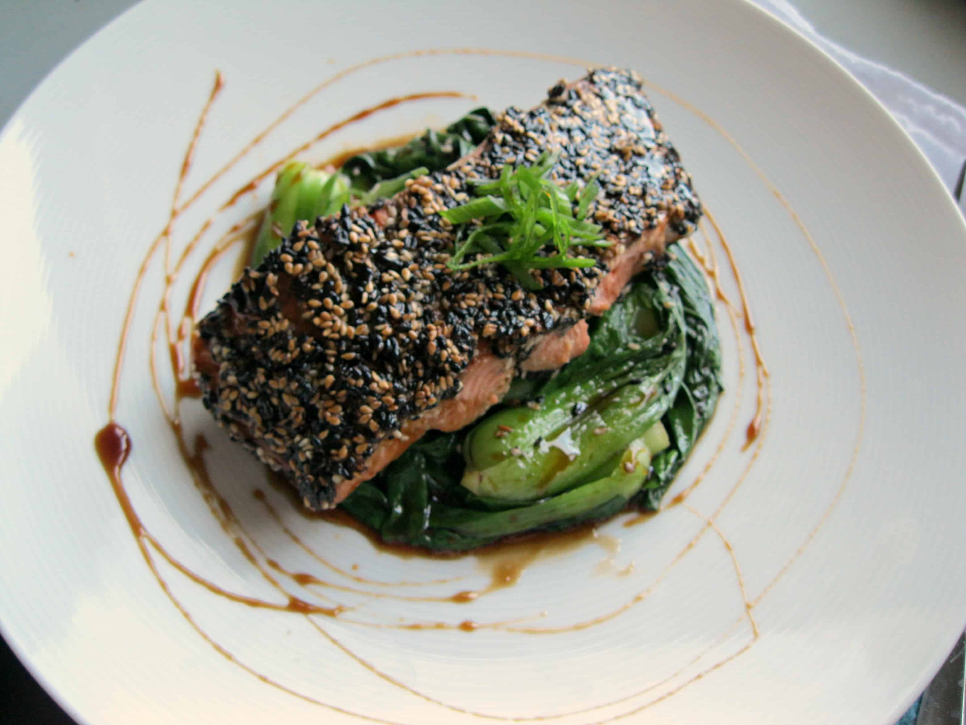 Top view of a sesame crusted salmon fillet over greens in a bowl.