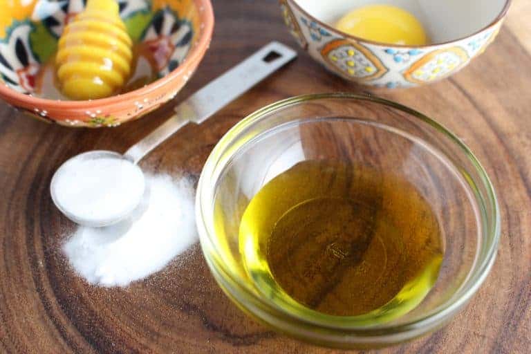 A small glass prep bowl of olive oil ext to a tablespoon of sugar.