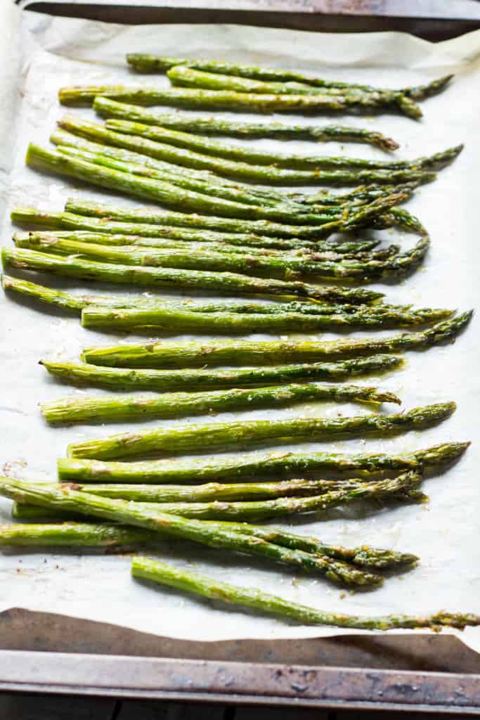 A row of roasted asparagus stalks on a baking tray.