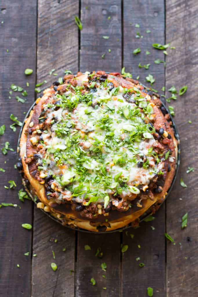 Top view of a taco cake on a wood table topped with sour cream and green onions.
