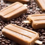 Angled side view of frozen coffee popsicles on a backdrop of coffee beans, emphasizing the popsicles' creamy texture and bold espresso color.