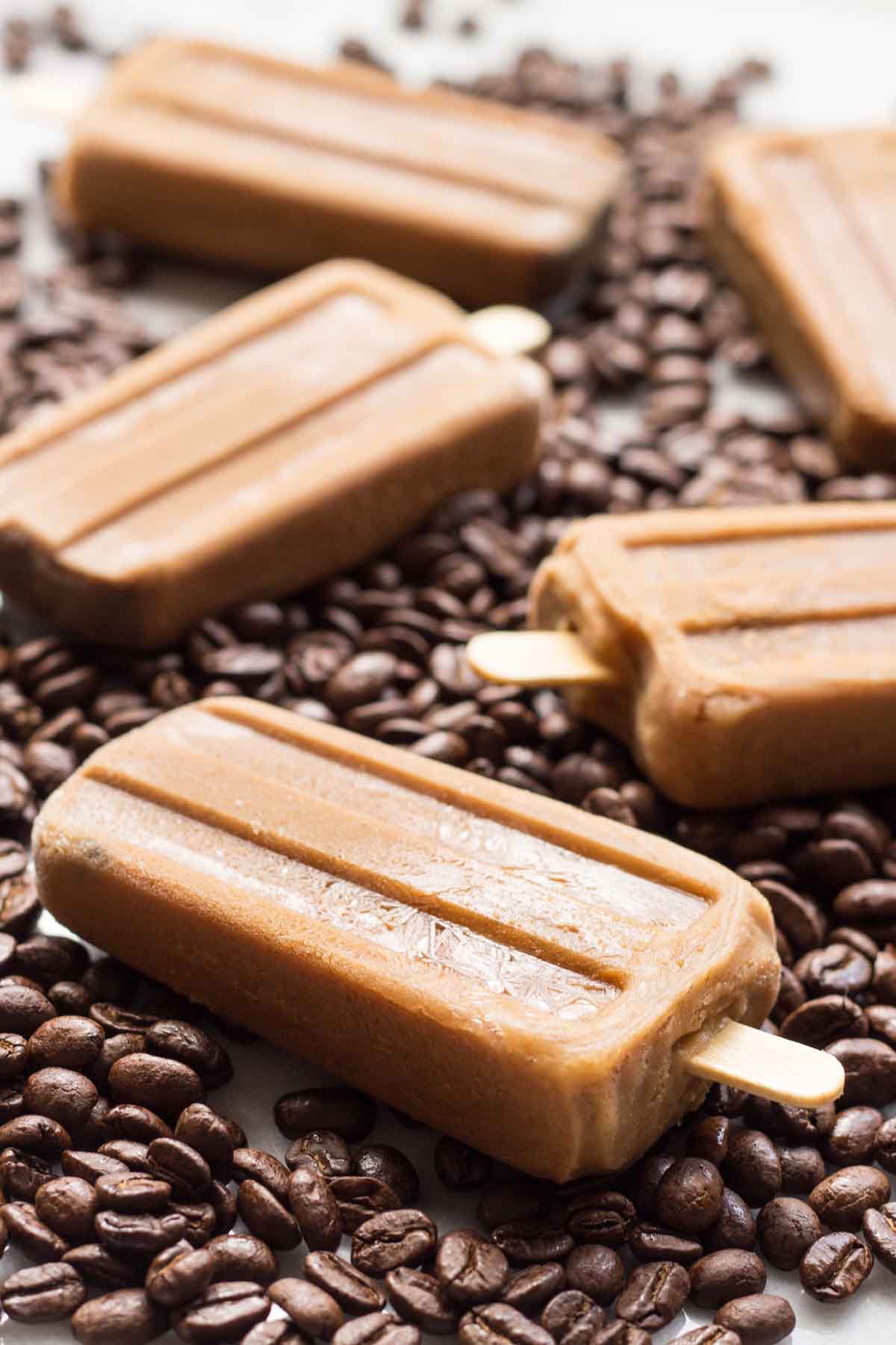 Angled side view of frozen coffee popsicles on a backdrop of coffee beans, emphasizing the popsicles' creamy texture and bold espresso color.