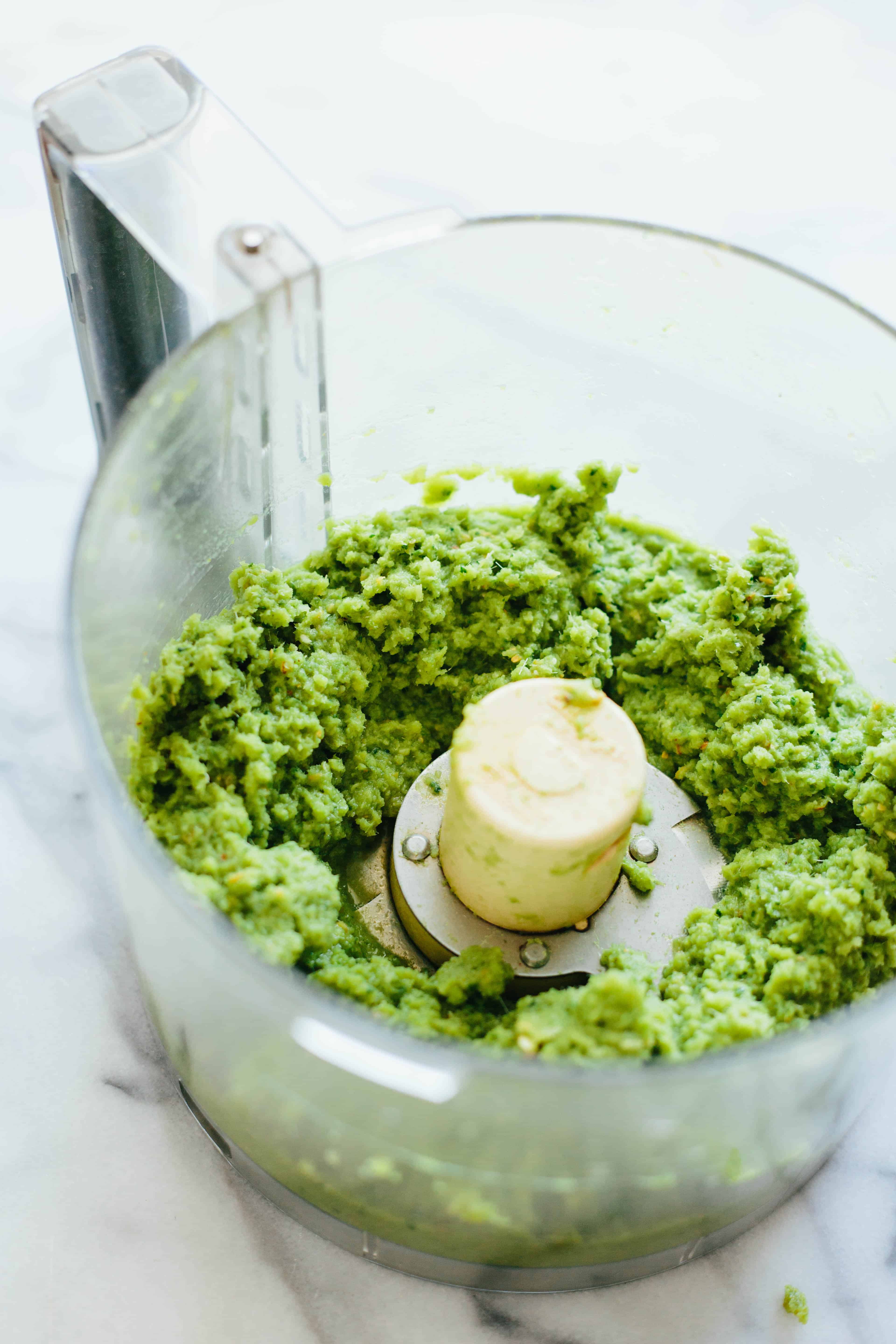 The bowl of a food processor with green herbs inside for curry sauce.