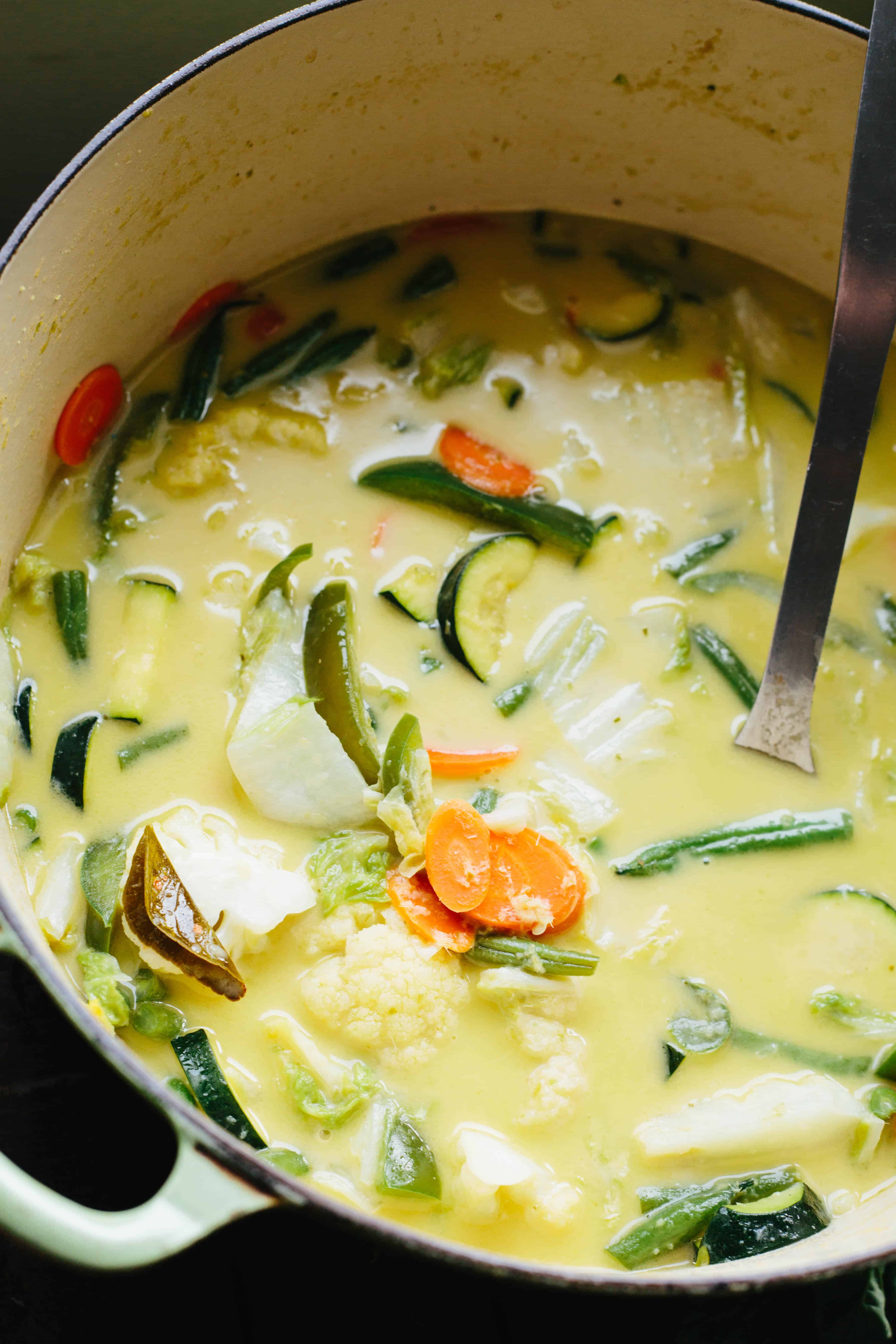 A ladle stirring a cast iron pot of Thai green curry.