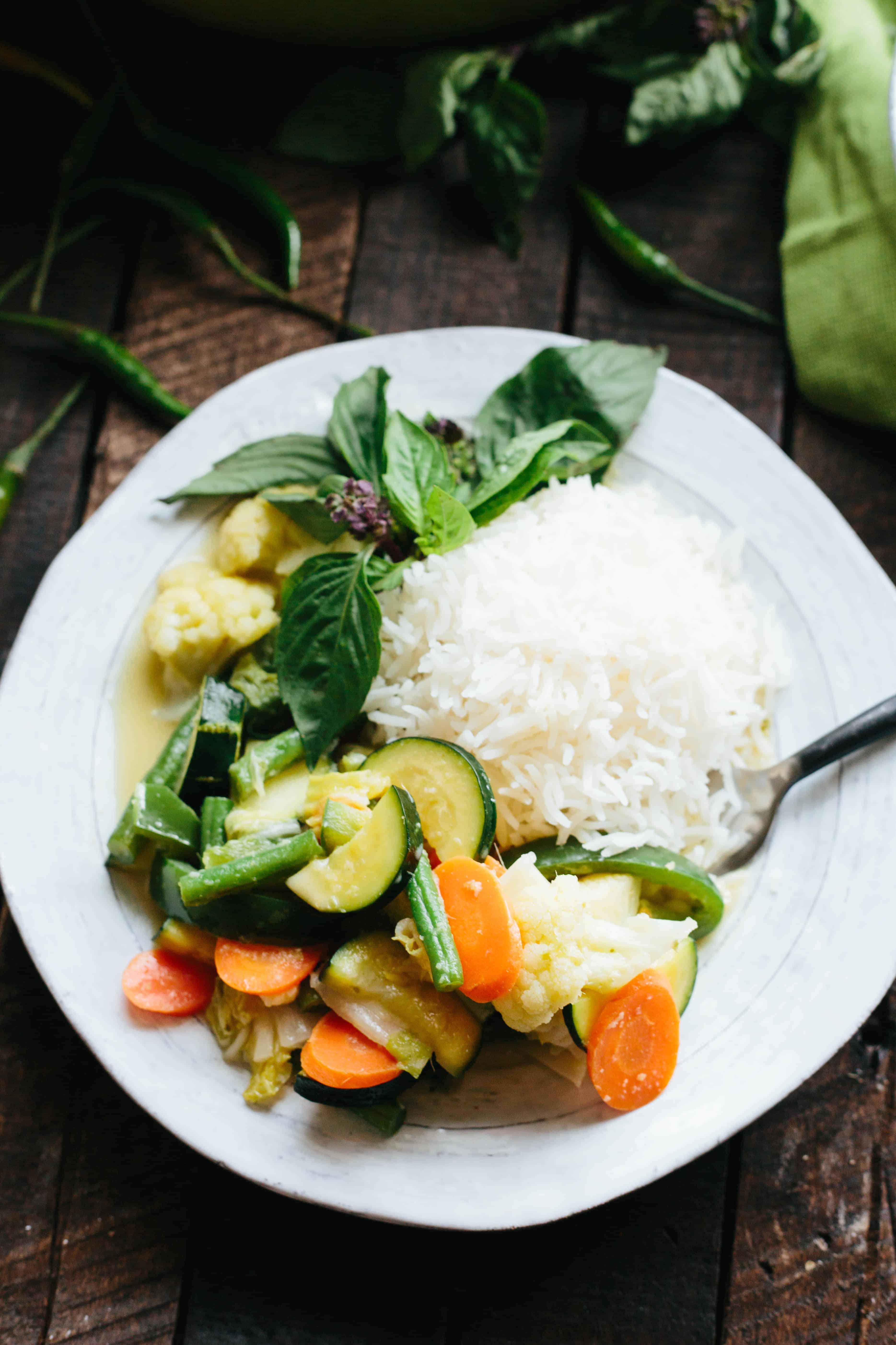 Close up top view of Thai green curry, rice, and fresh basil on a white diner plate.