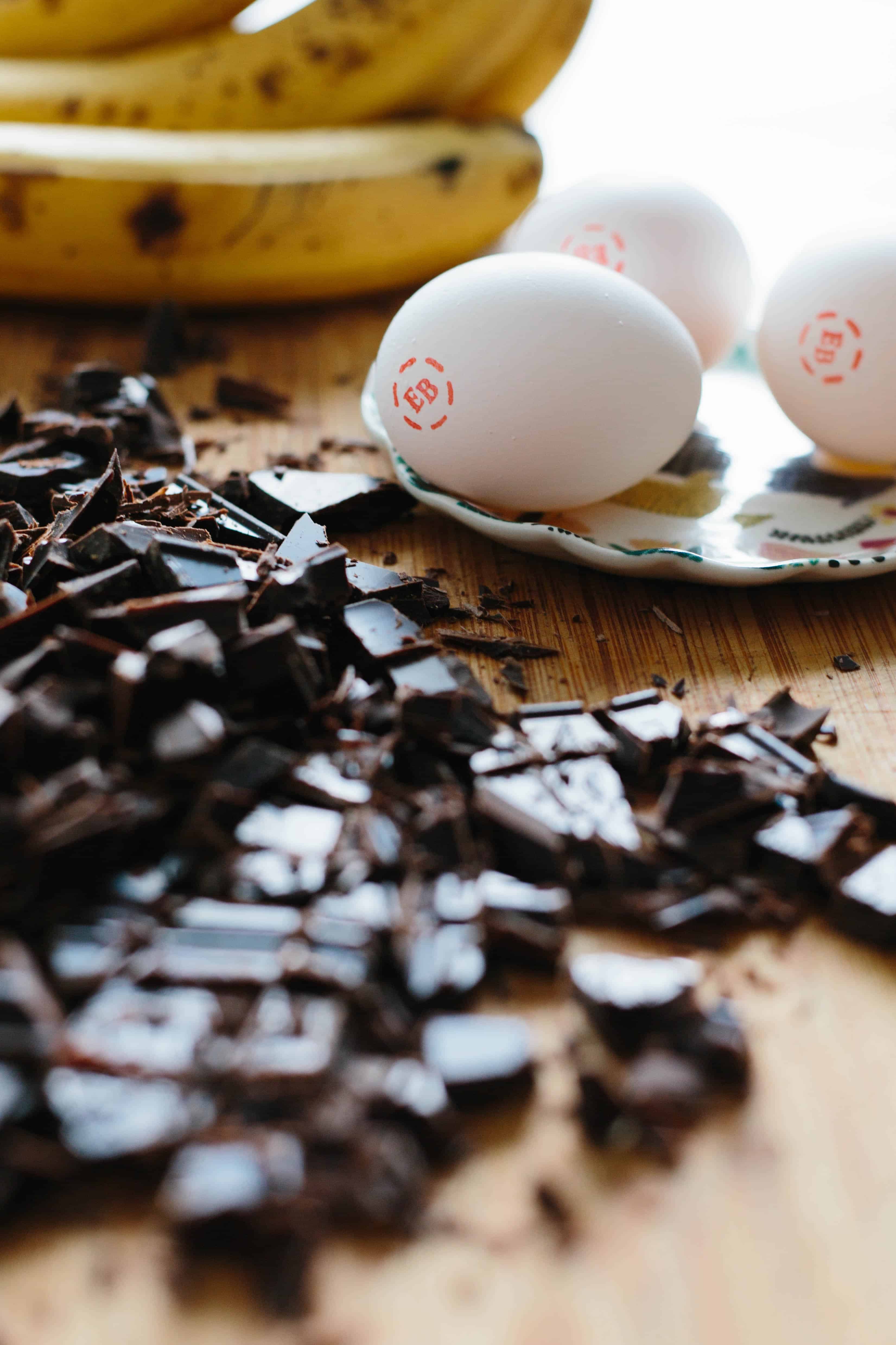 Close up up of roughly chopped chocolate and three fresh eggs.