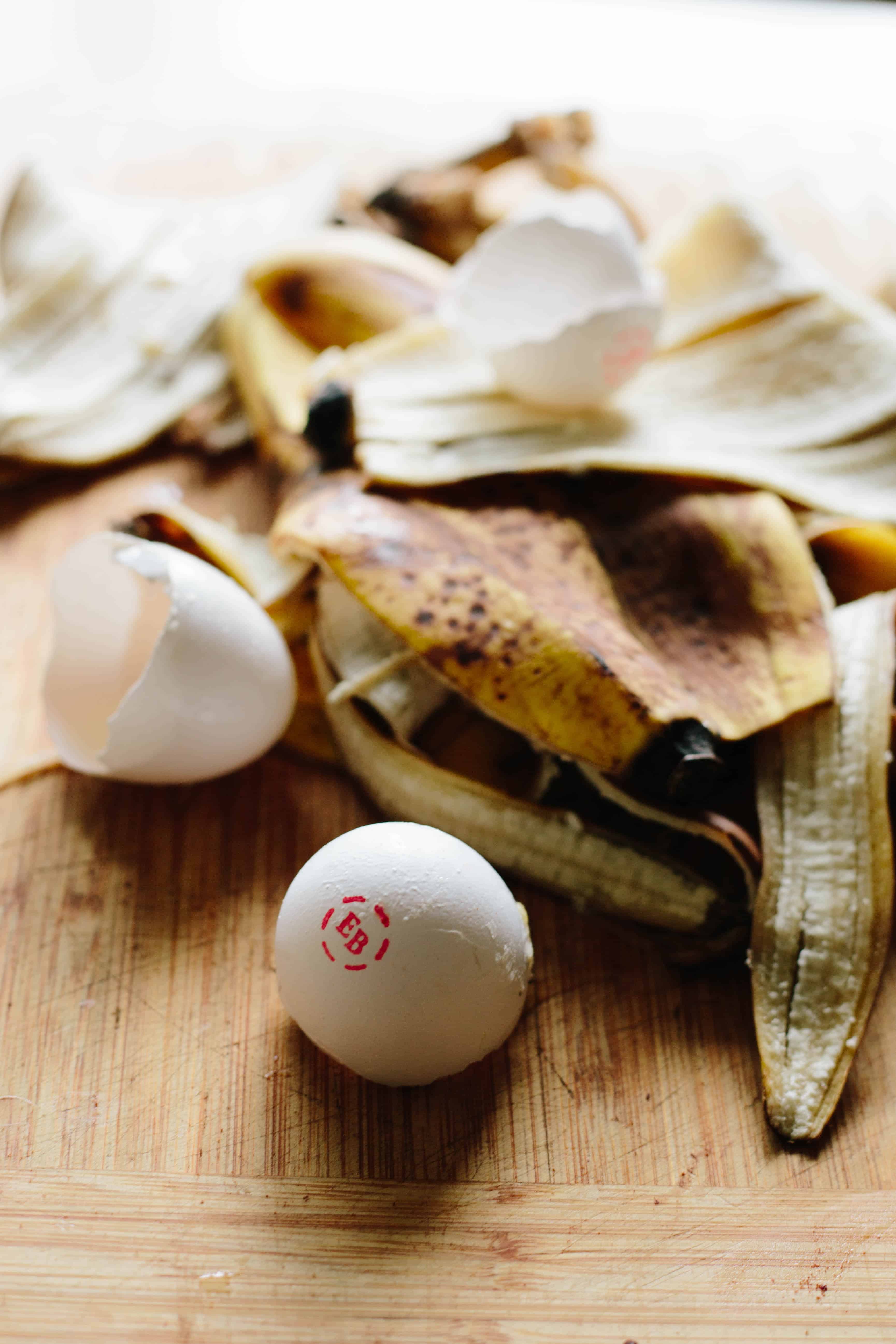 Banana peels and egg shells on a wooden cutting board.
