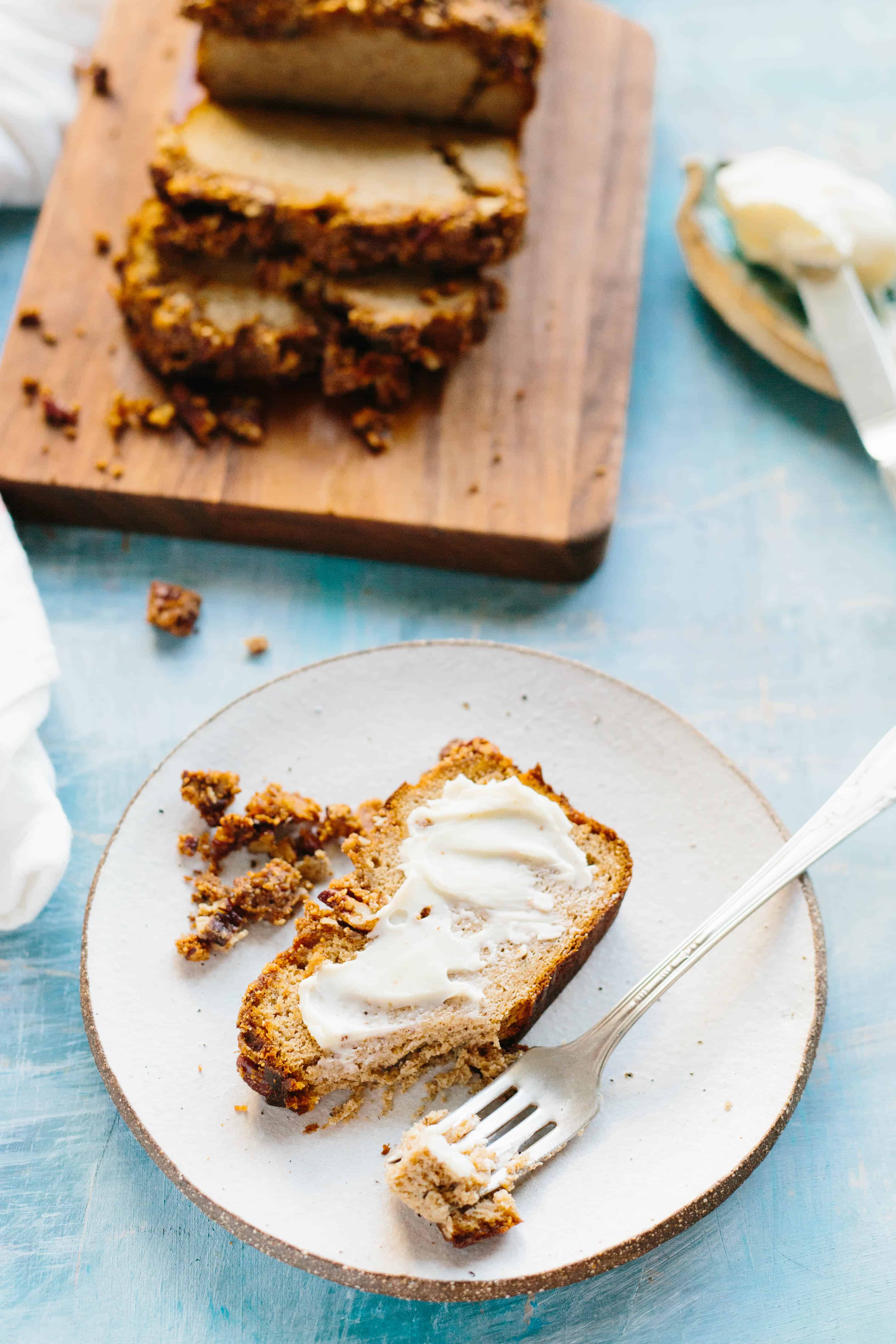 A buttered slice of Paleo banana bread on a small plate with a fork.