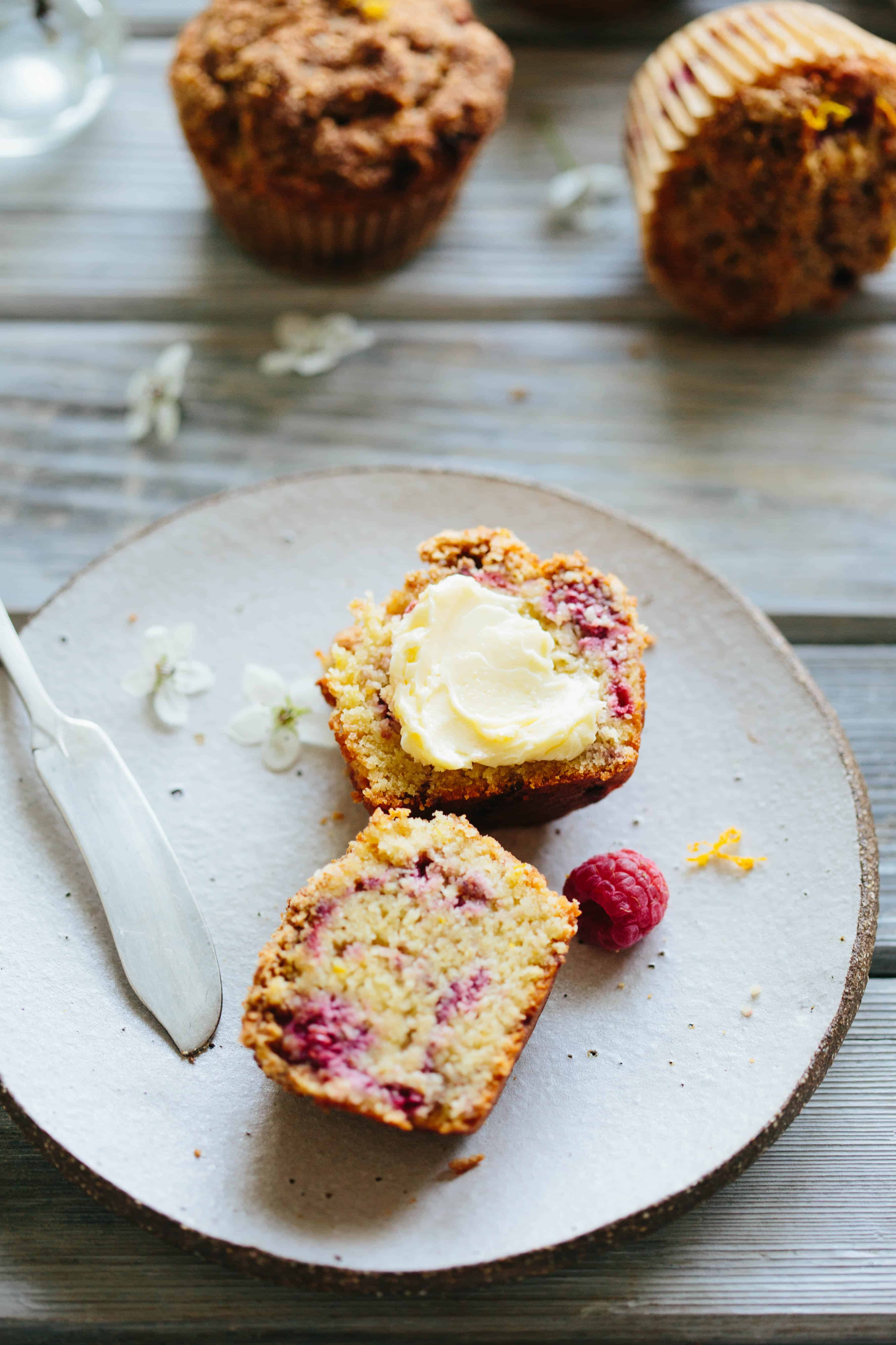 Top view of a split and buttered orange raspberry Paleo muffin on a white plate.