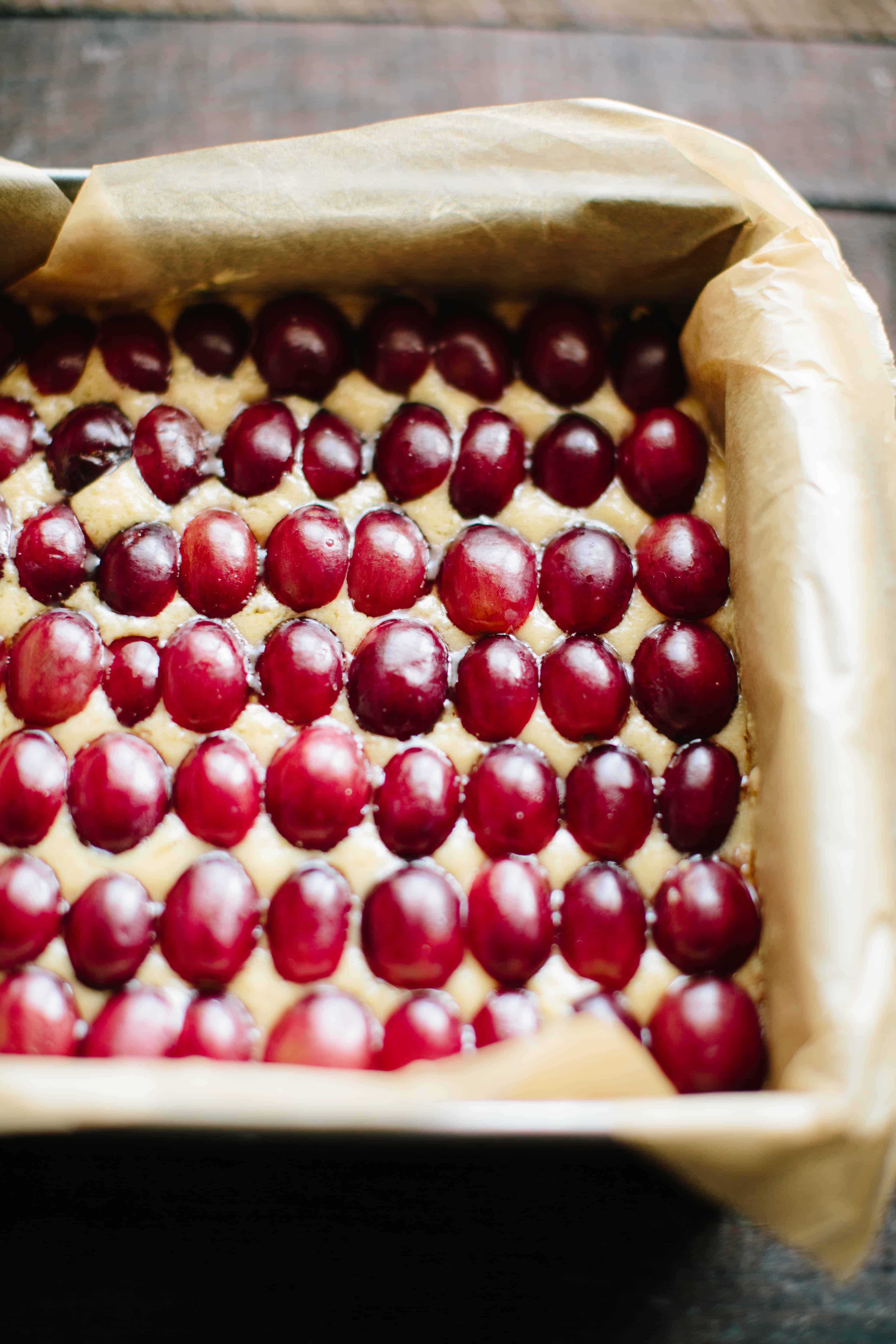 Parchment lined baking pan filled with peanut butter shortbread batter that has red grapes pressed into it in rows.
