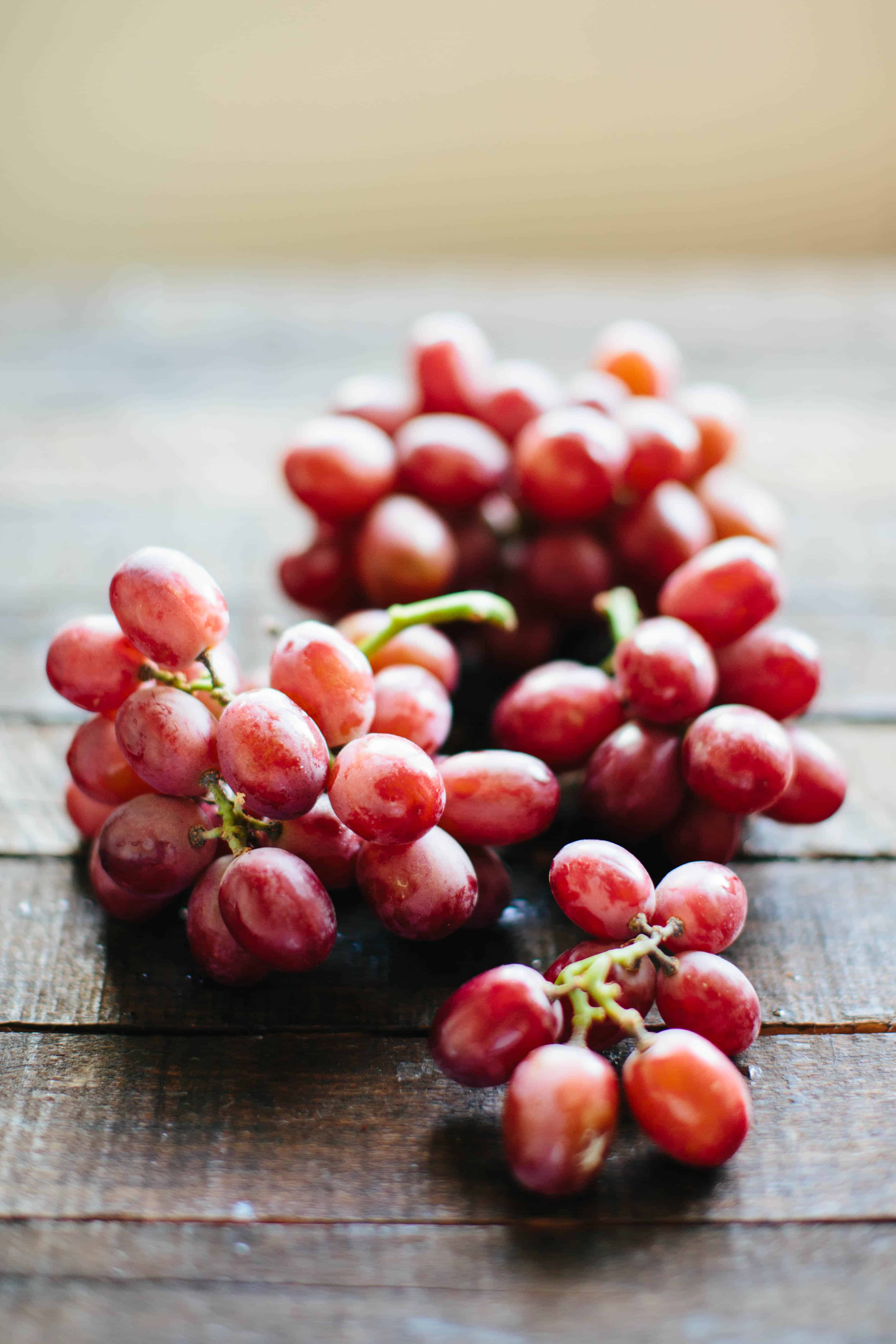 A bunch of delicious looking red grapes placed on a wood plank table.
