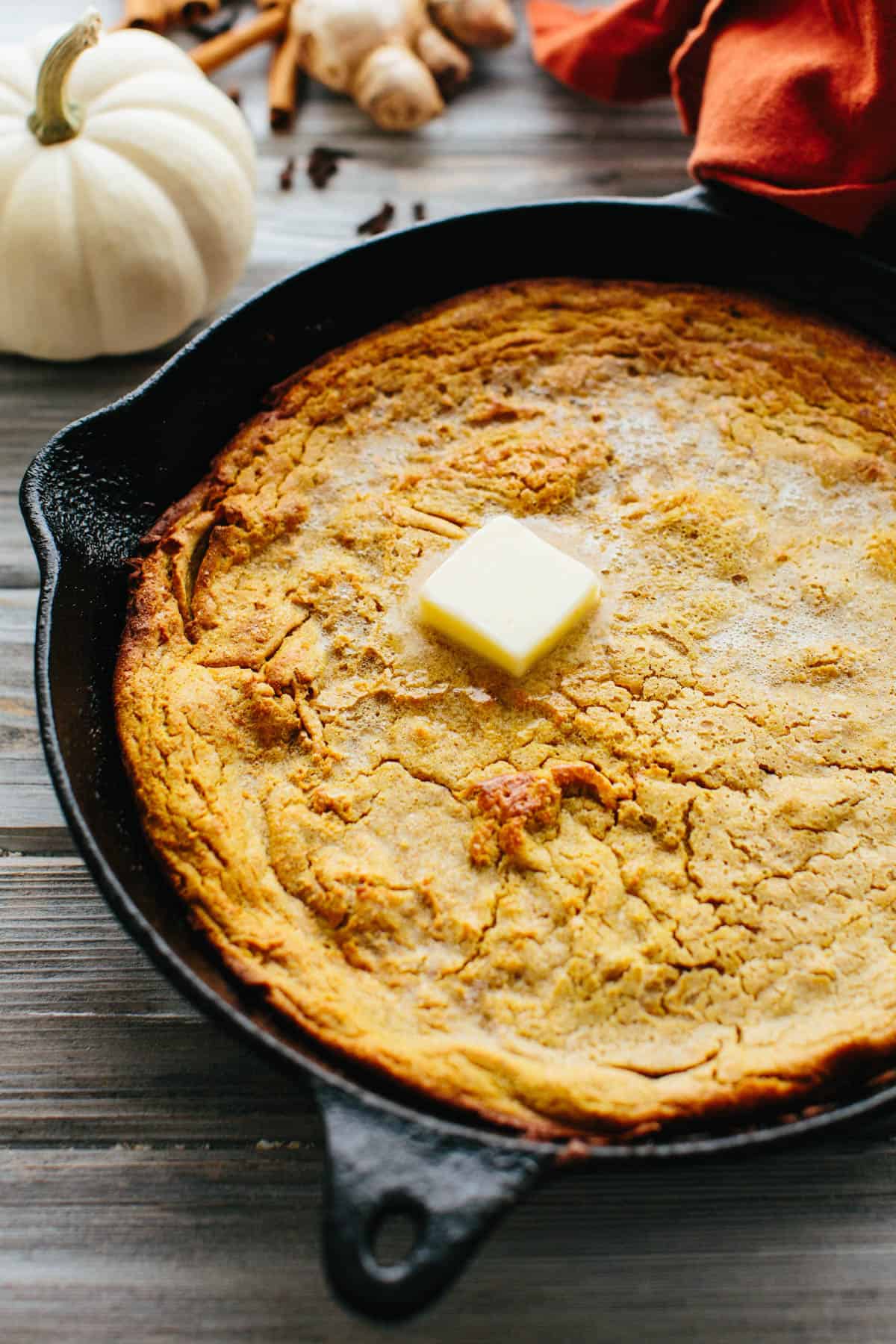 Close up of A cast iron skillet with pumpkin Dutch baby with a pat of melting butter