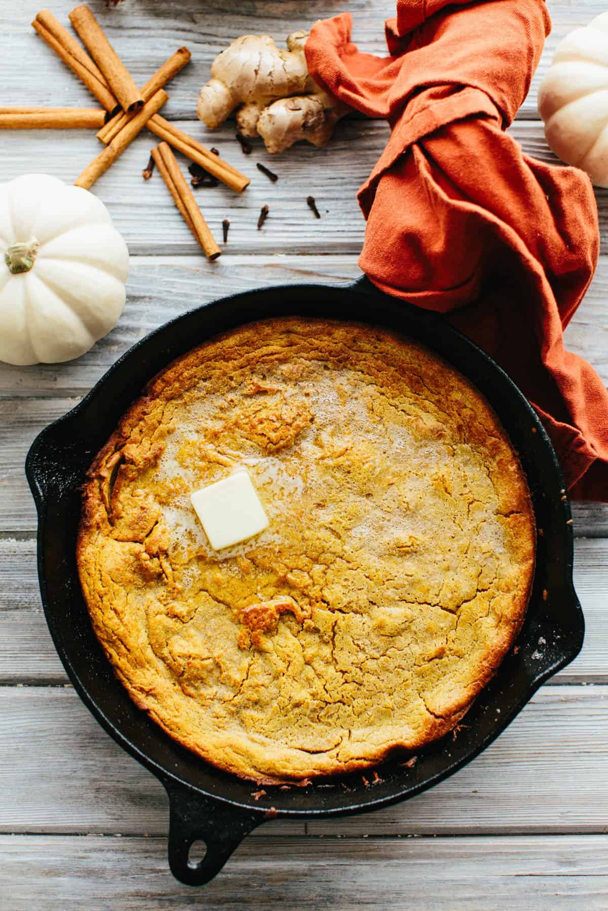 A cast iron skillet with pumpkin Dutch baby with a pat of melting butter