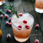 glass of light pink drink with ice, fresh cranberries and rosemary on dark wooden background