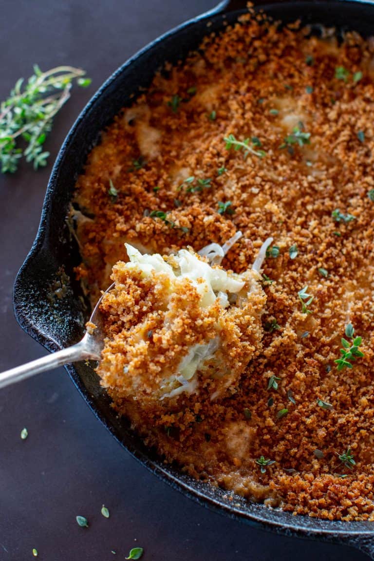 spoon full of fennel onion gratin in a cast iron skillet with fresh thyme
