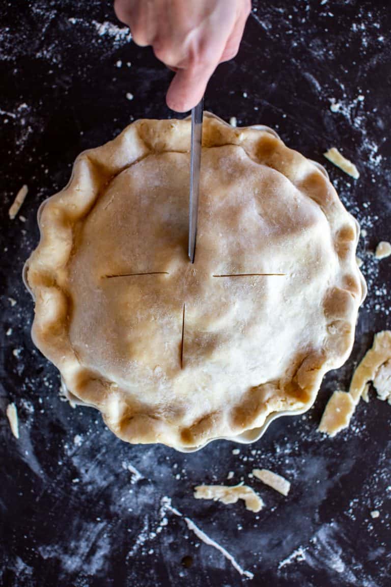 overhead shot of a hand cutting vents in an unbaked pie