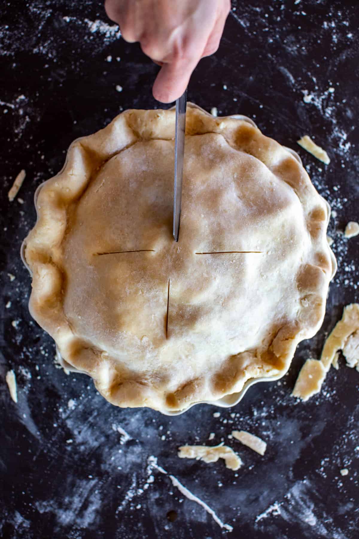 overhead shot of a hand cutting vents in an unbaked pie