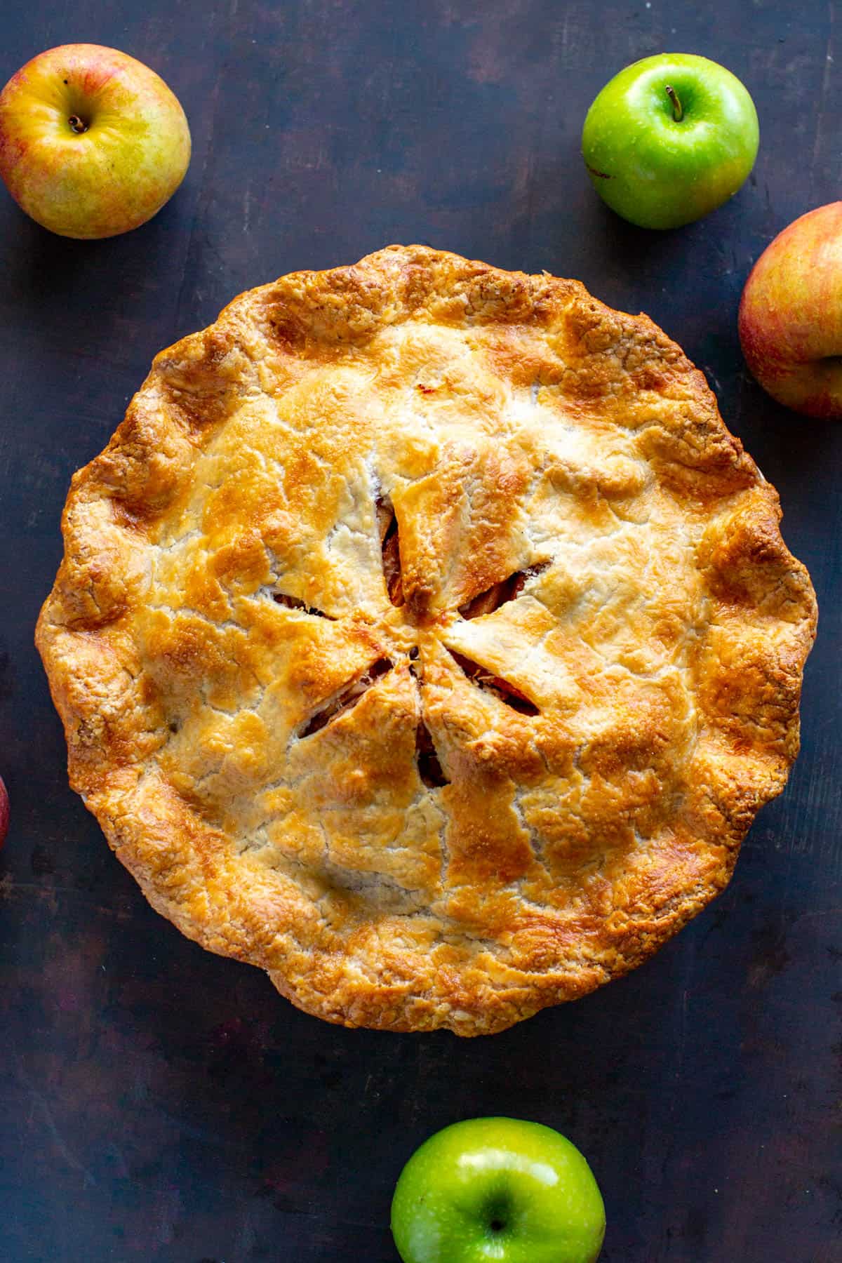 top view of a whole baked apple pie with apples scattered around