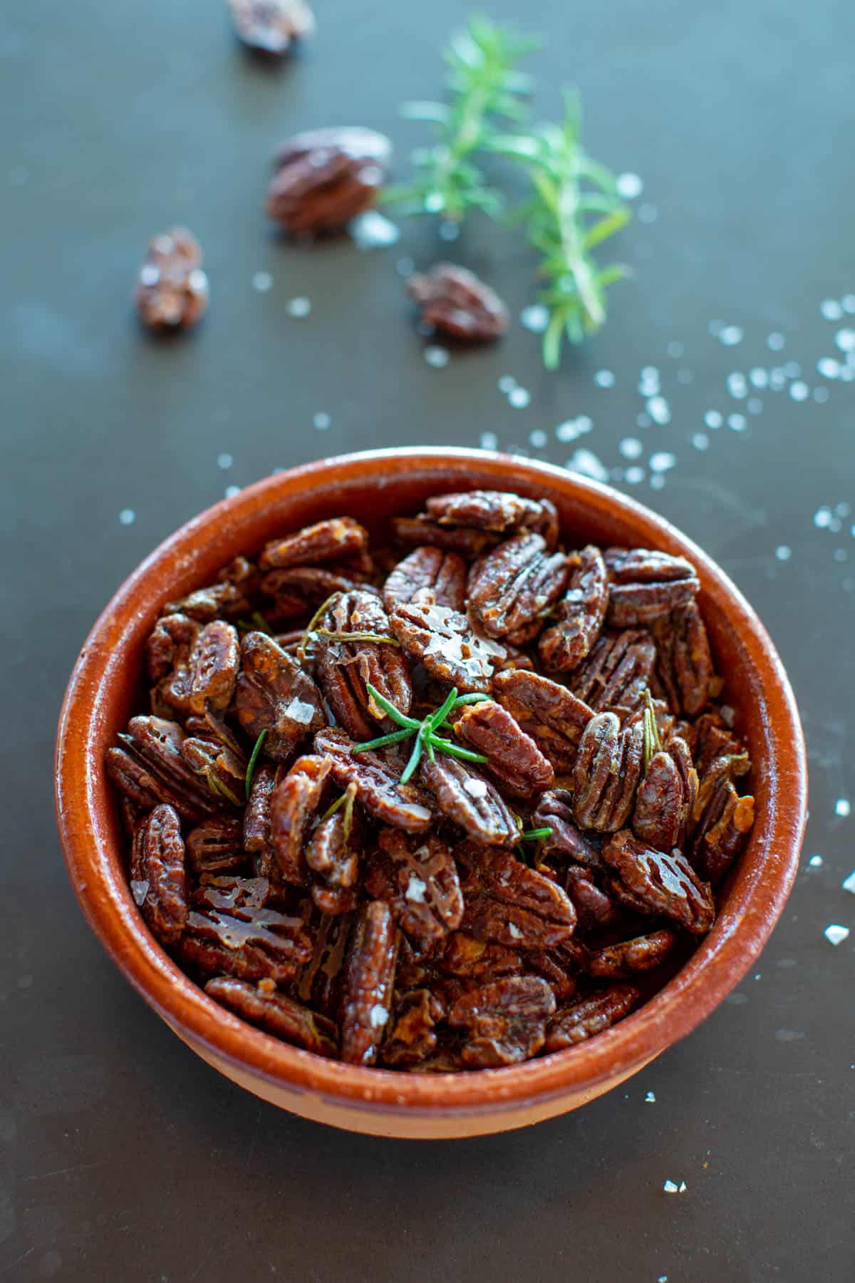 terra cotta bowl of rosemary roasted maple pecans on dark background