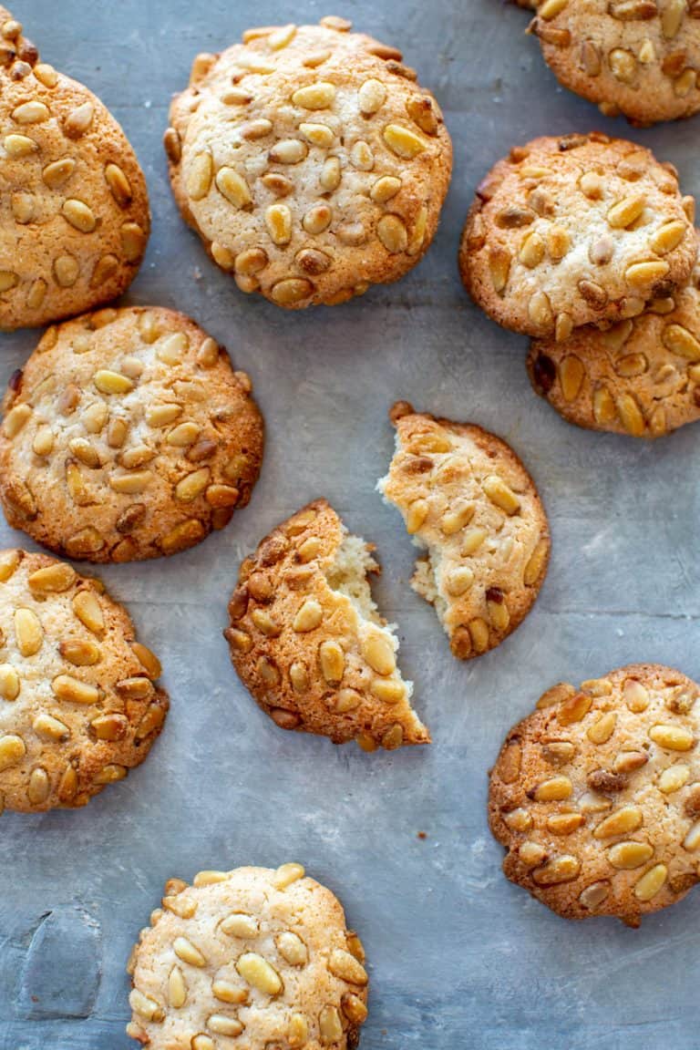 broken pignoli cookie on a gray surface surrounded by more cookies