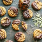Top view of peanut butter cookies dipped in chocolate and sprinkled with sea salt spread out on a wood tabletop.