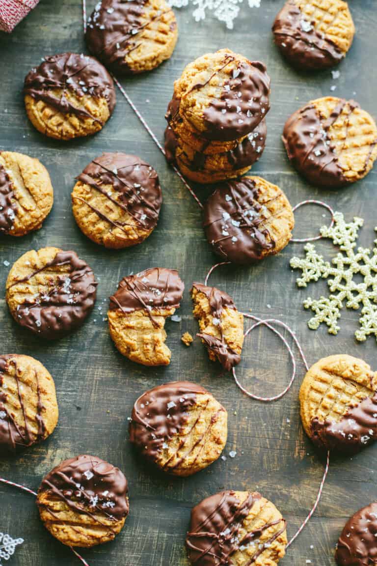 Top view of peanut butter cookies dipped in chocolate and sprinkled with sea salt spread out on a wood tabletop.