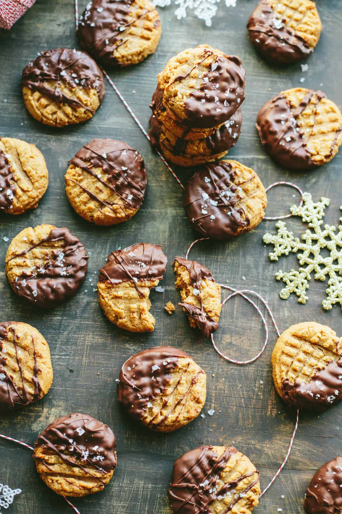 Top view of peanut butter cookies dipped in chocolate and sprinkled with sea salt spread out on a wood tabletop.
