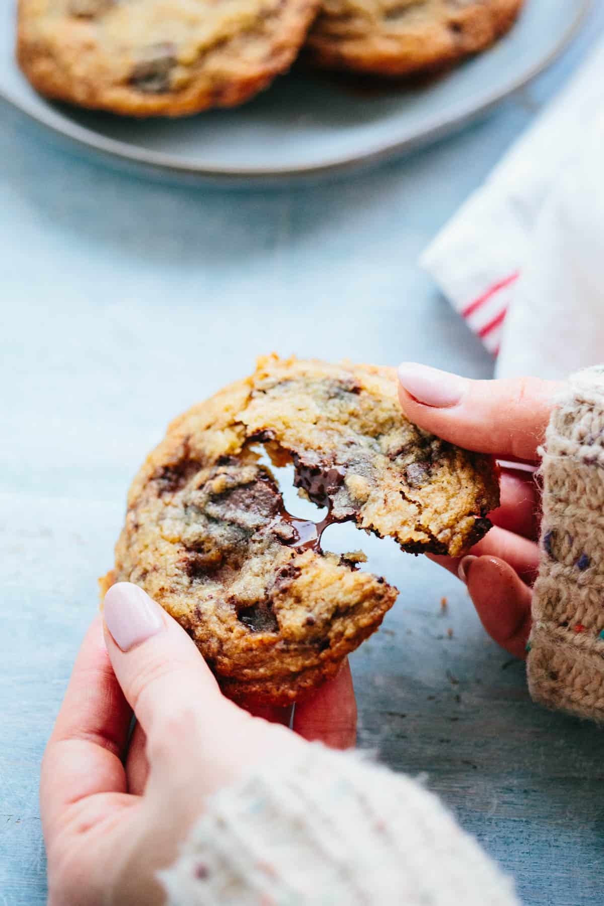 Two hands breaking apart a chocolate toffee chunk cookie with melted chocolate