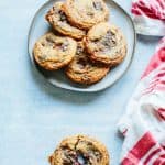 A plate of chocolate toffee chip cookies with one cookie broken apart in the foreground