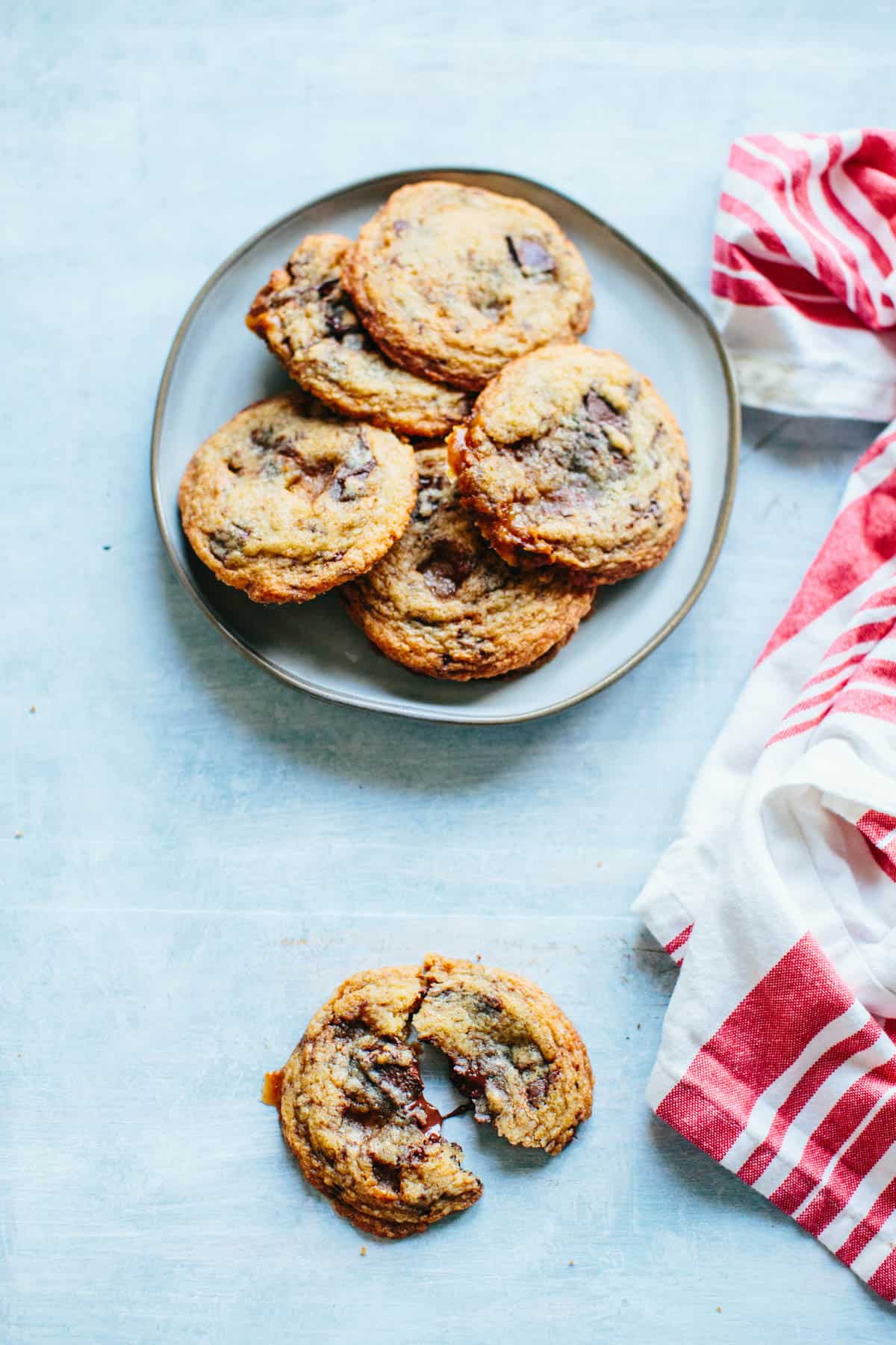 A plate of chocolate toffee chunk cookies with one cookie broken apart in the foreground