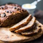 front view of a loaf of cinnamon raisin walnut bread with a few slices on a cutting board