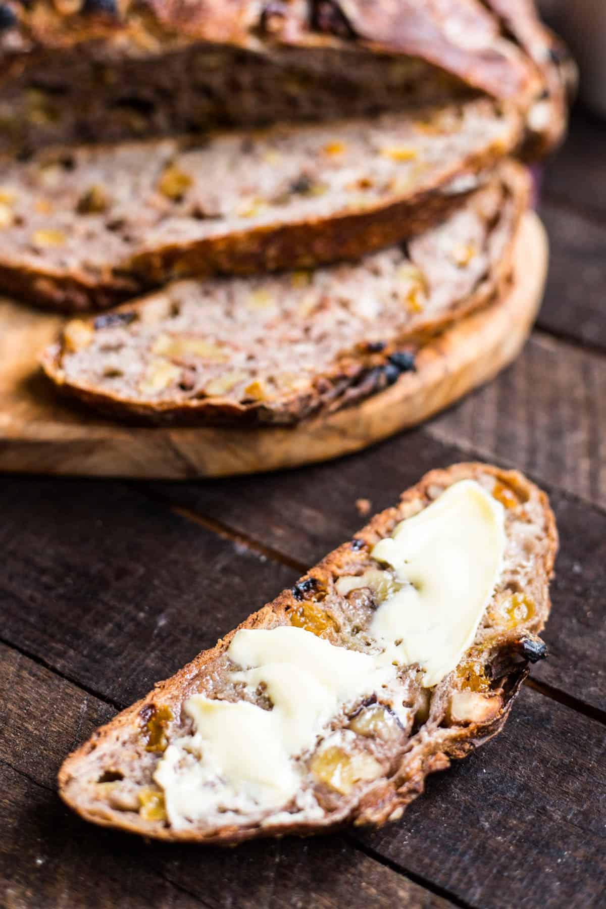 slices of cinnamon raisin walnut bread, one in the foreground with butter