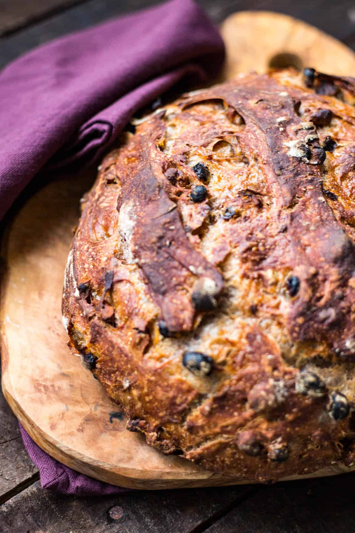 Loaf of cinnamon raisin walnut bread on a cutting board with purple napkin