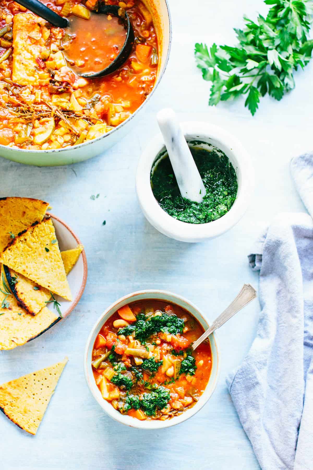 overhead shot of a table with a pot of minestrone, a bowl of minestrone and a mortar and pestle of pistou