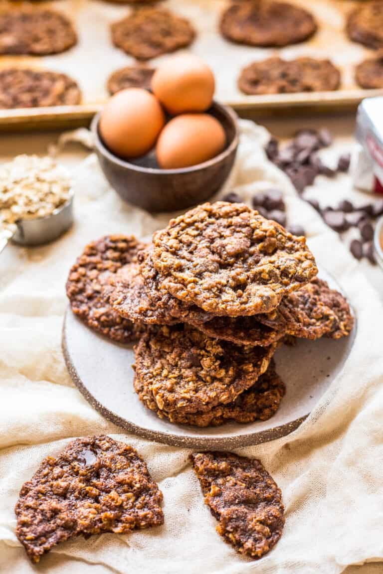 a plate of cookies with a broken cookie in the foreground and ingredients in the background