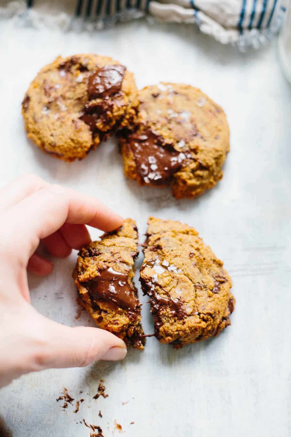 A hand breaking a Paleo chocolate chip cookie in half.