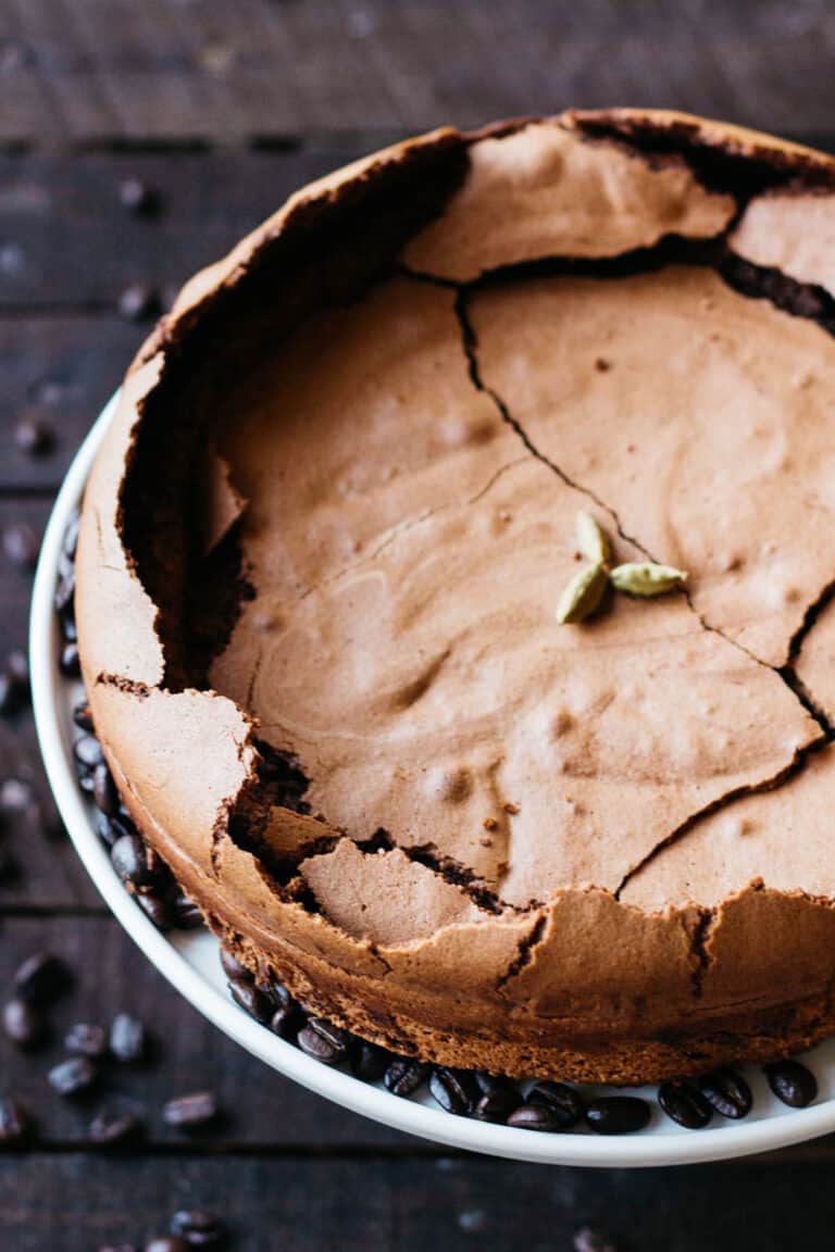 Top view of a flourless chocolate cake with a cracked top and cardamom pods