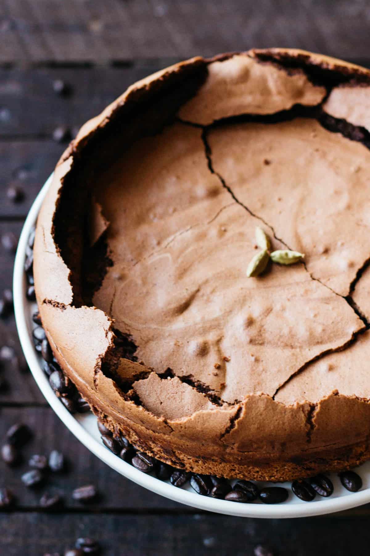 Top view of a flourless chocolate cake with a cracked top and cardamom pods