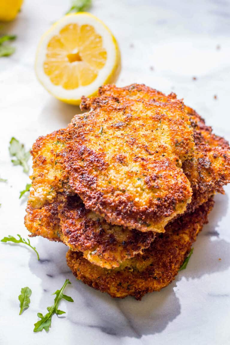 A stack of thin crispy Italian breaded chicken breasts with a lemon.