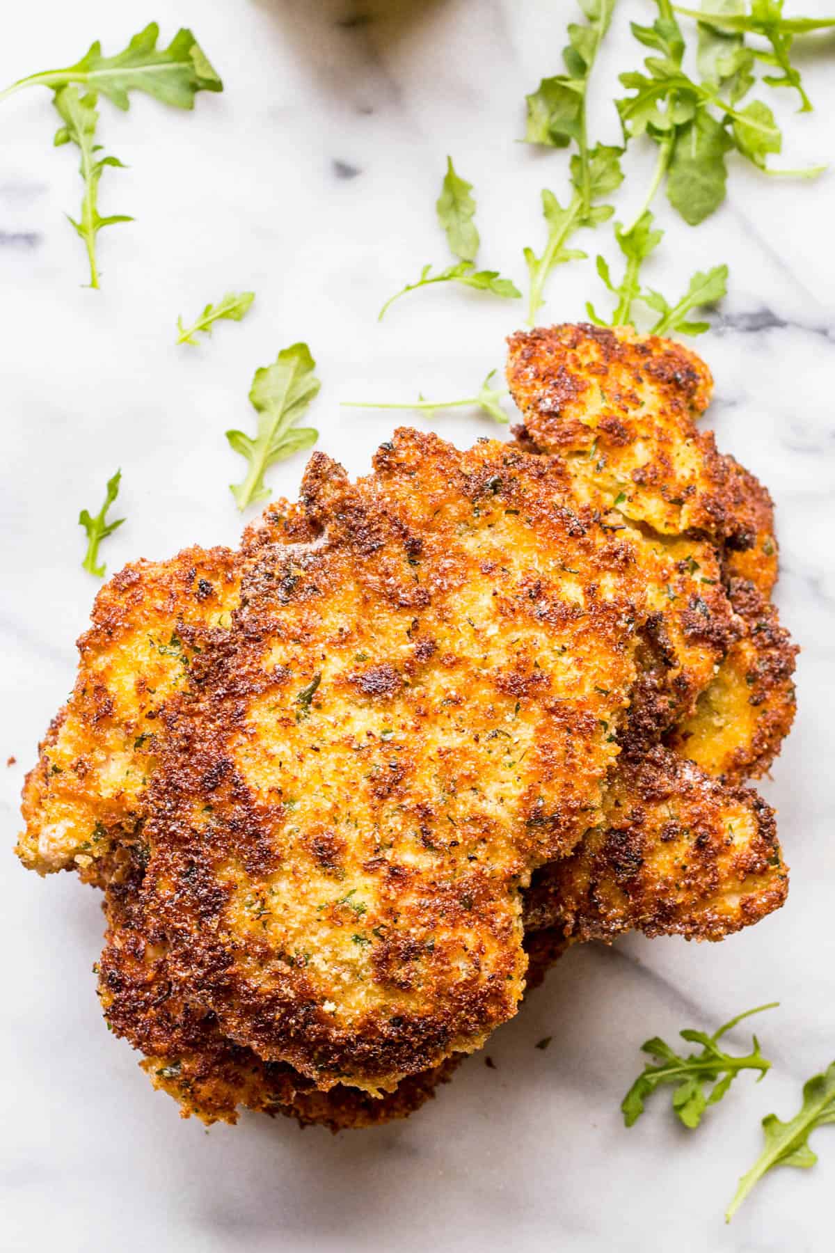 Crispy pan fried Italian breaded chicken cutlets stacked with arugula scattered beneath.