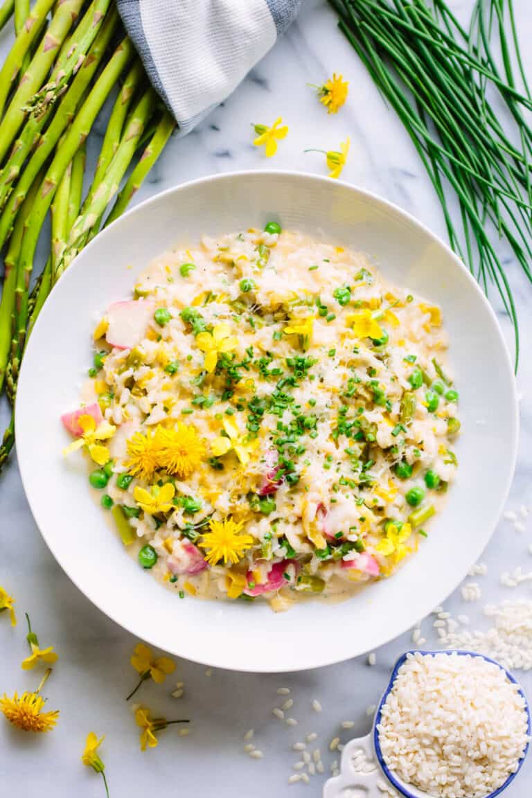 overhead shot of vegetable risotto with asparagus, chives, and rice scattered in the background