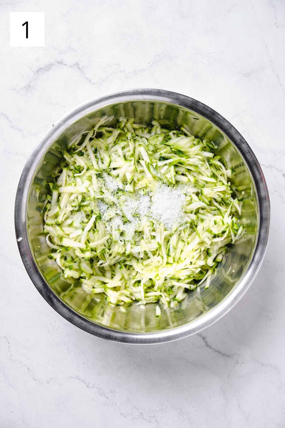 A bowl of grated zucchini with salt sprinkled on top.