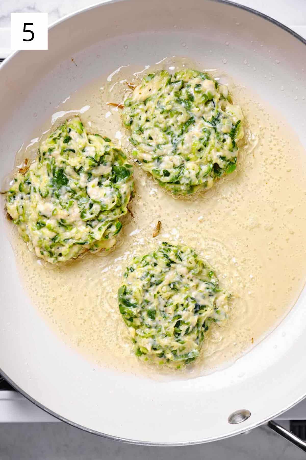 A pan of raw zucchini fritter batter frying.