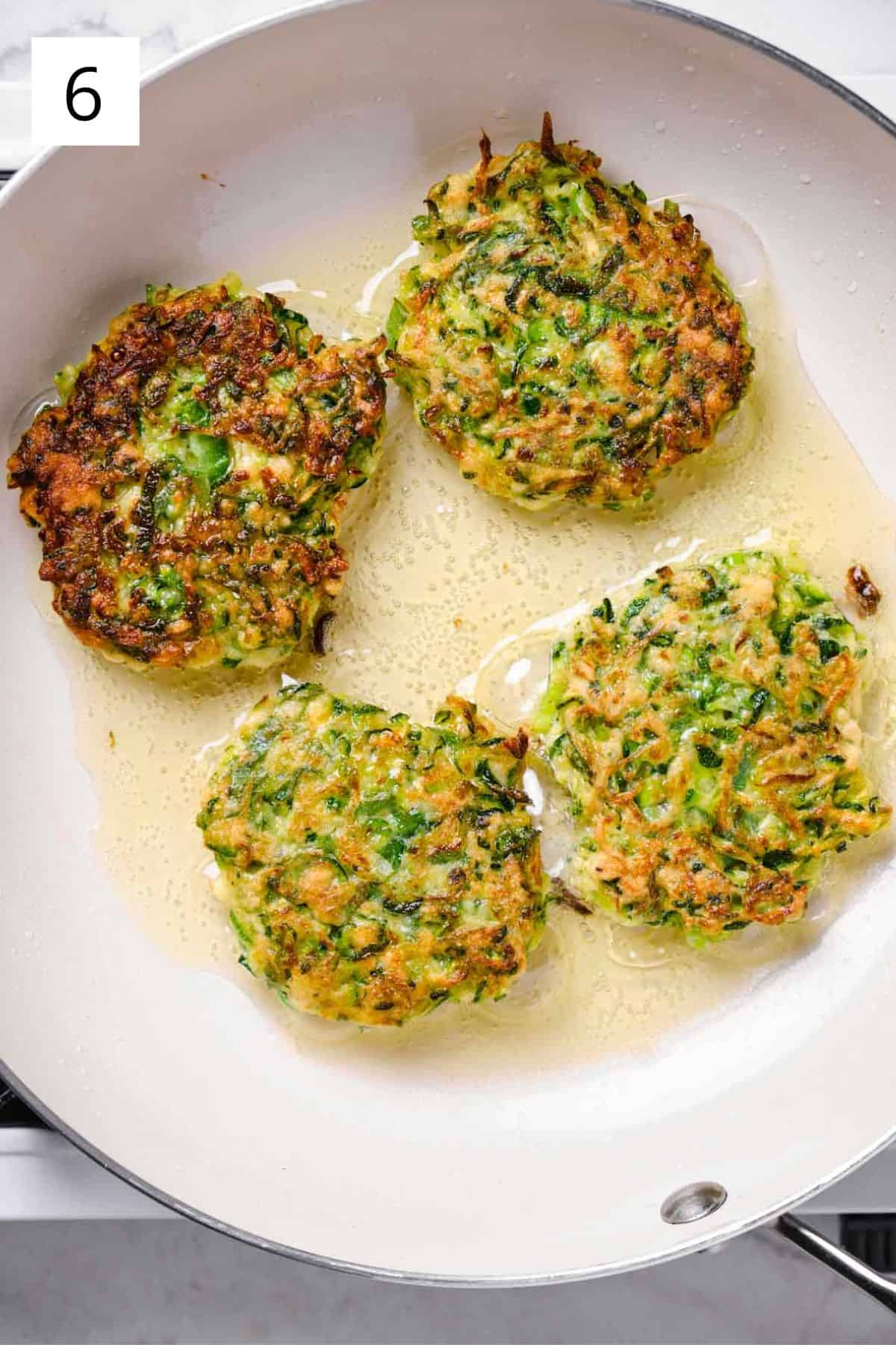 Zucchini fritters frying to golden brown in a pan.