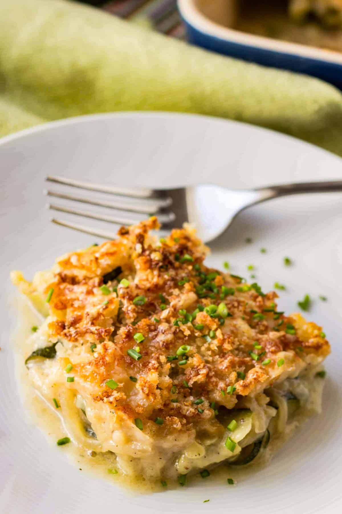 Close up of a serving of zucchini gratin on a white plate with a fork.