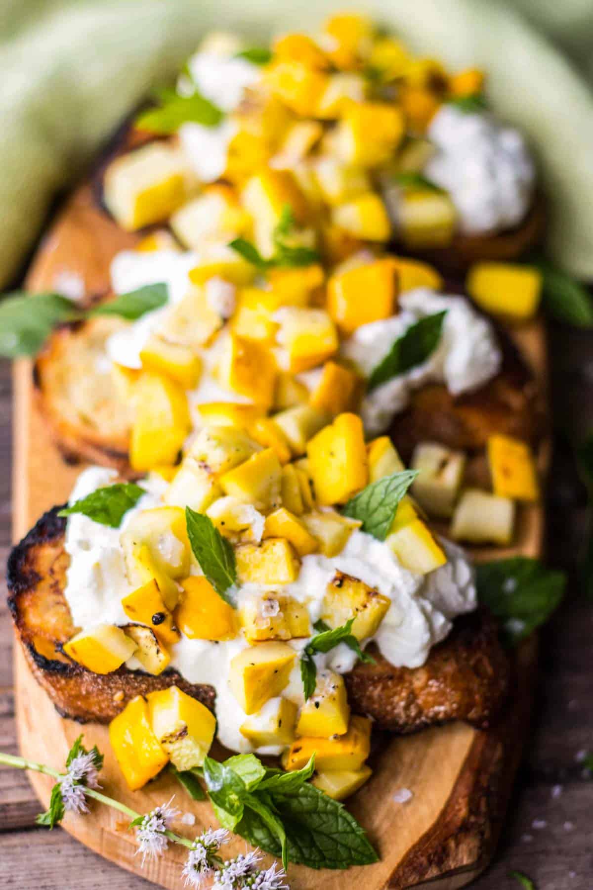 wooden platter with 3 pieces of toast with grilled yellow zucchini and ricotta