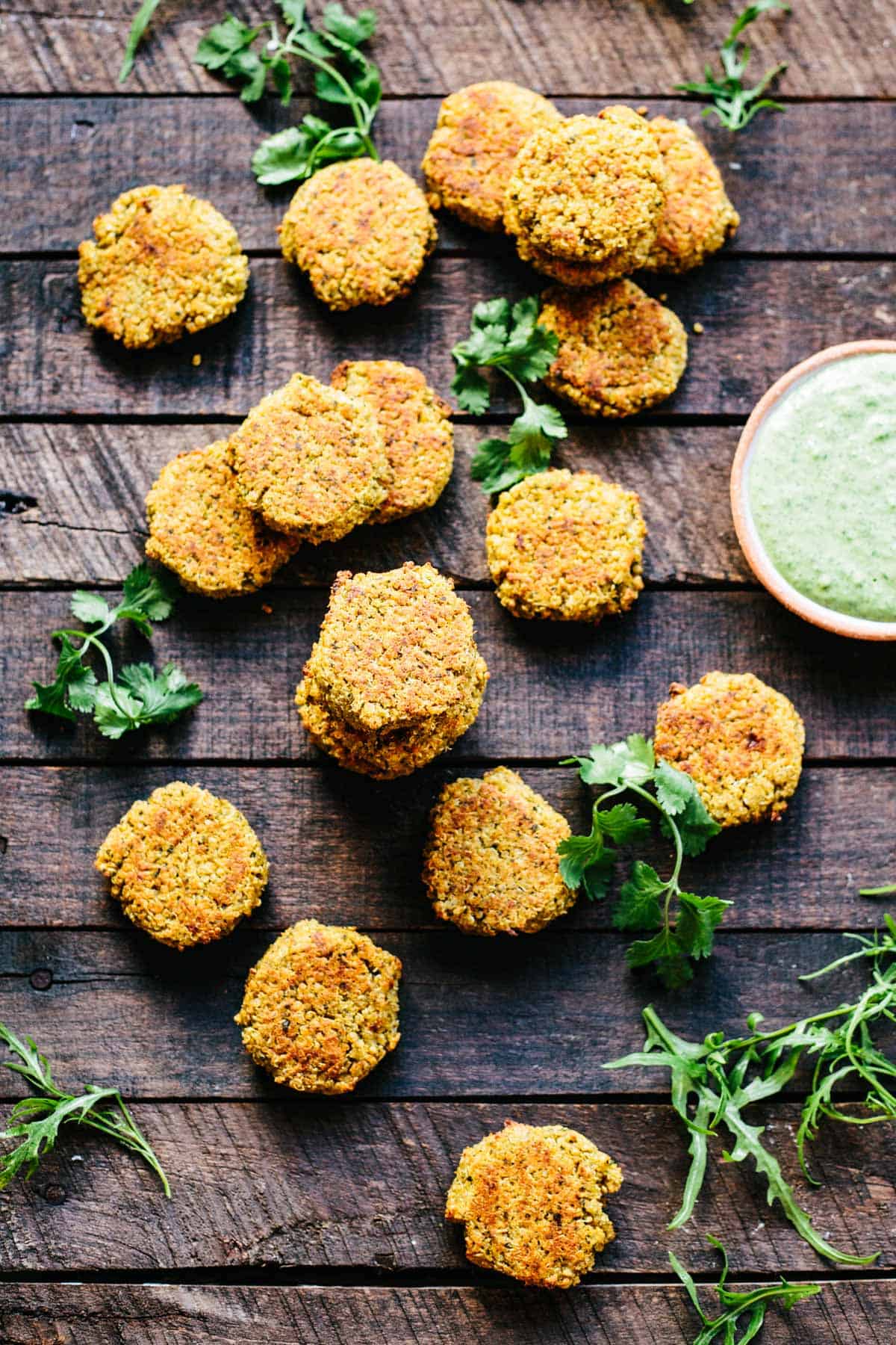 Quinoa falafel patties on a wood slat table next to a bowl of green tahini.