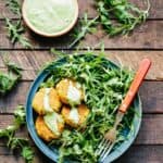Plate loaded with salad greens and quinoa falafel drizzled with green tahini.