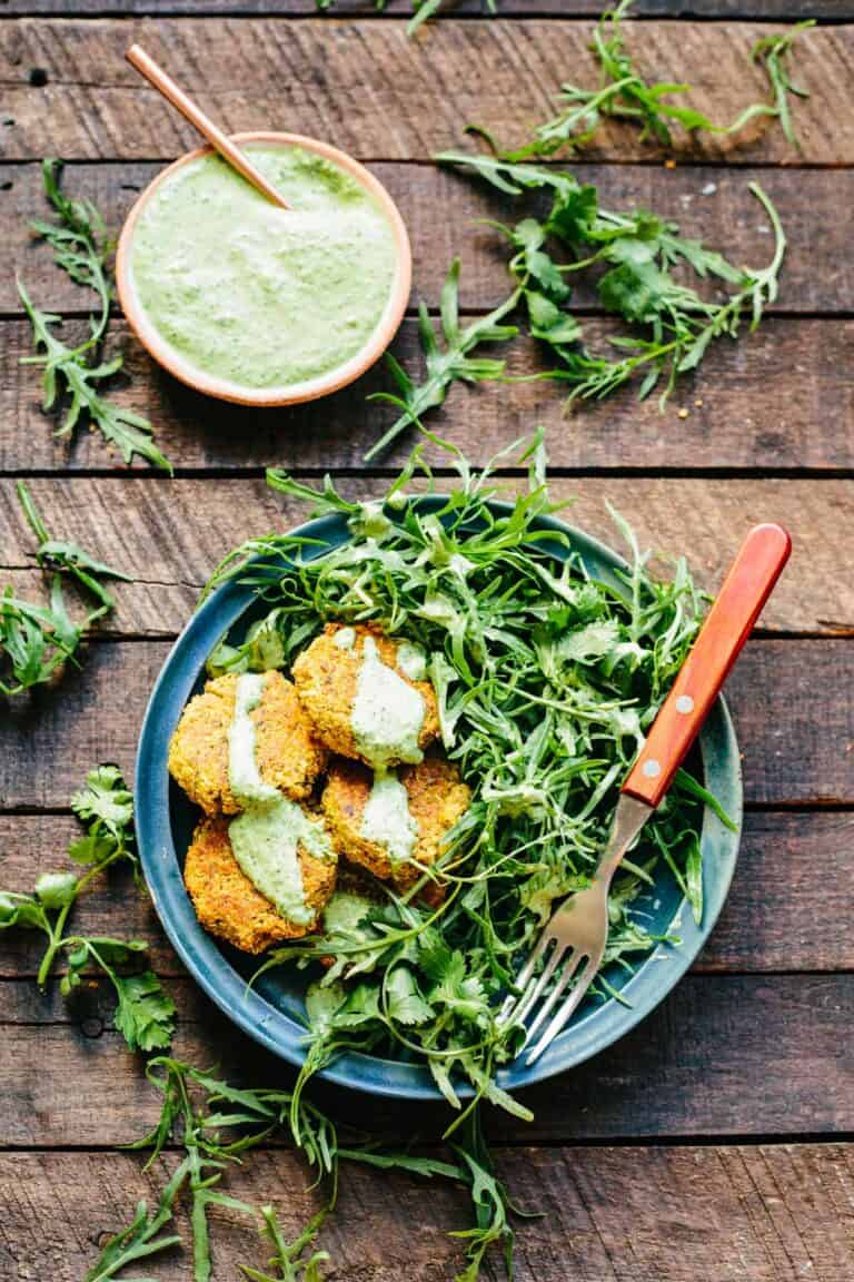 Plate loaded with salad greens and quinoa falafel drizzled with green tahini.